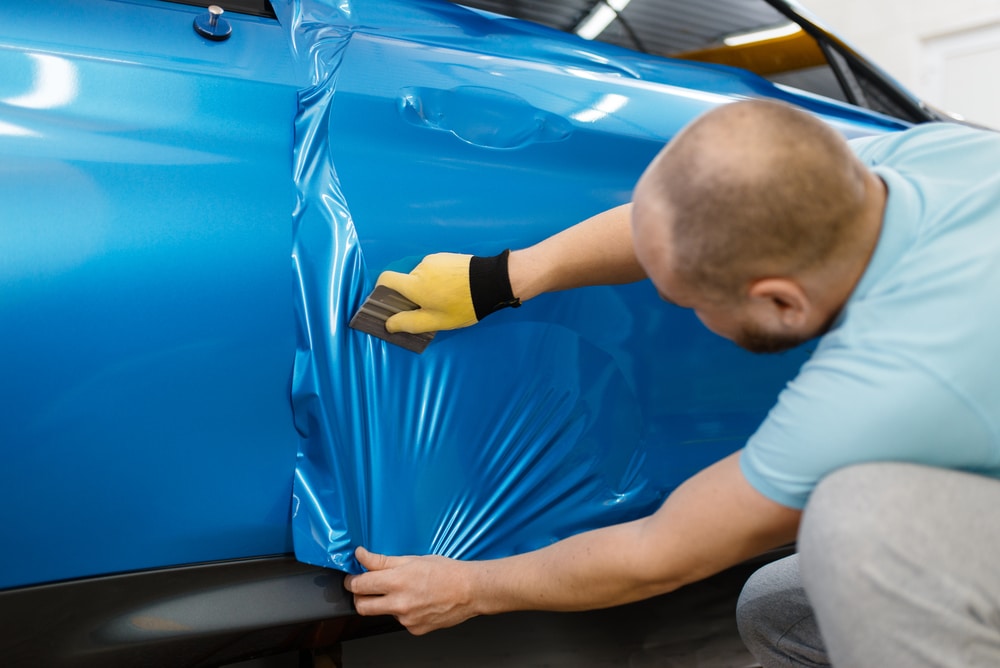 Un homme qui pose un covering bleu sur une voiture